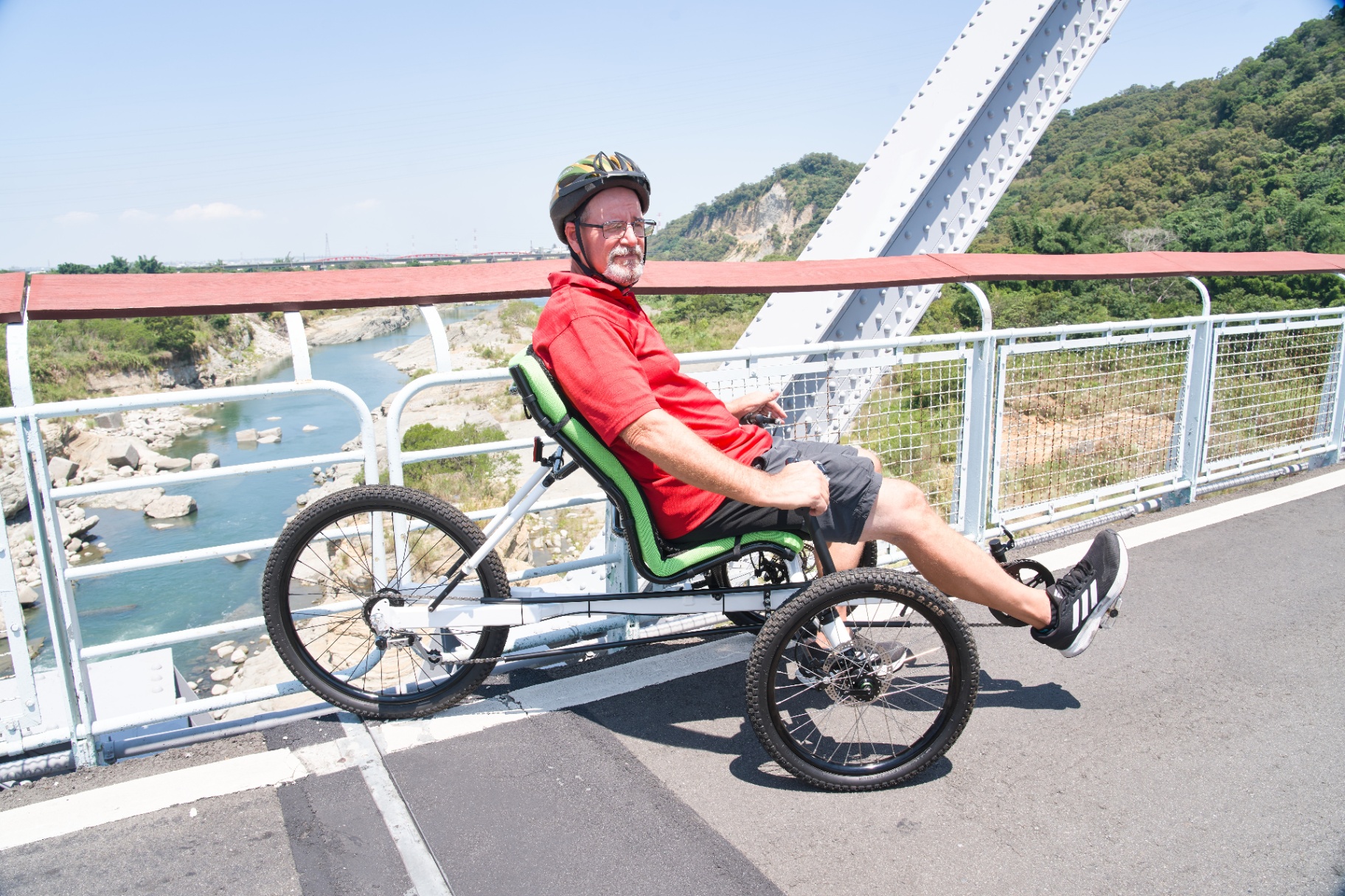 Rider on an OVELOX recumbent trike crossing a bridge in a relaxed reclined posture